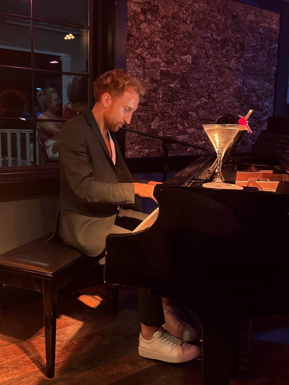 Étienne at a grand piano in a moody bar, martini resting on the lid